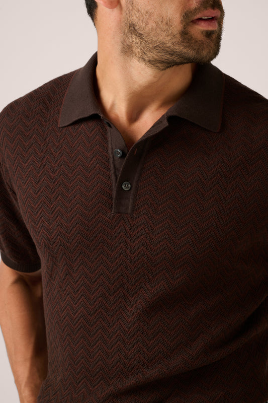 Man wearing a brown patterned polo shirt against a neutral background