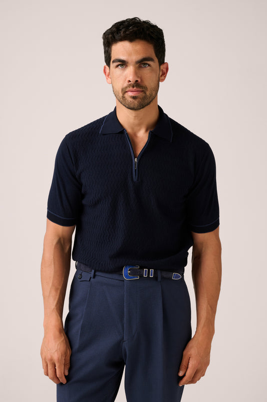 Man wearing a navy polo shirt and pants against a plain background