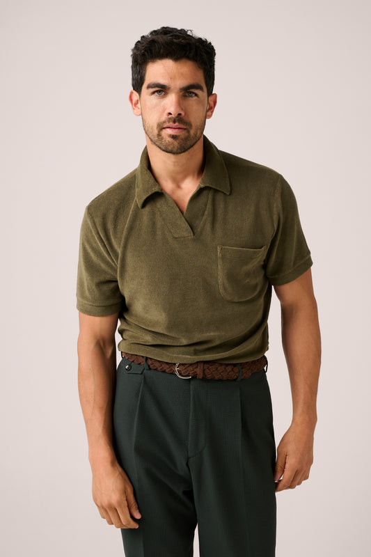 Man wearing an olive green polo shirt and dark pants on a plain background