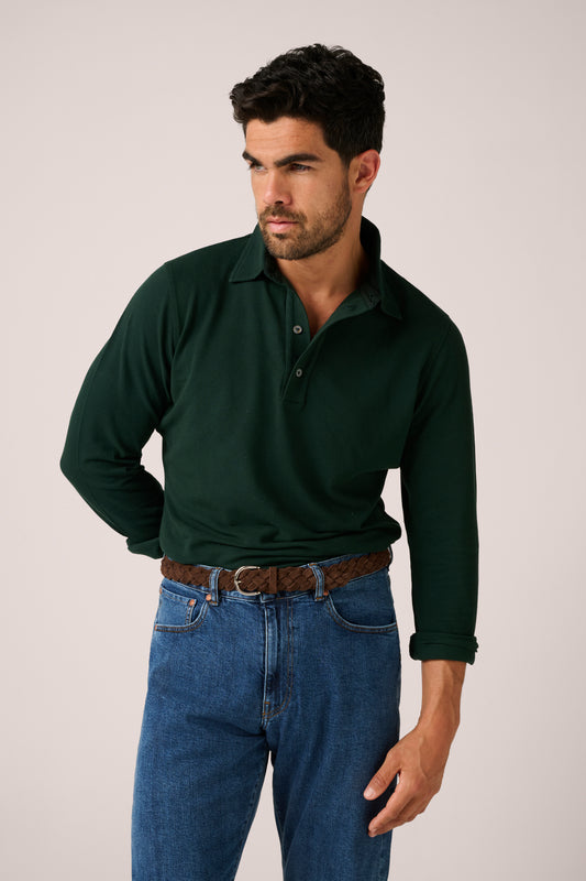 Man wearing a dark green polo shirt and blue jeans against a plain background