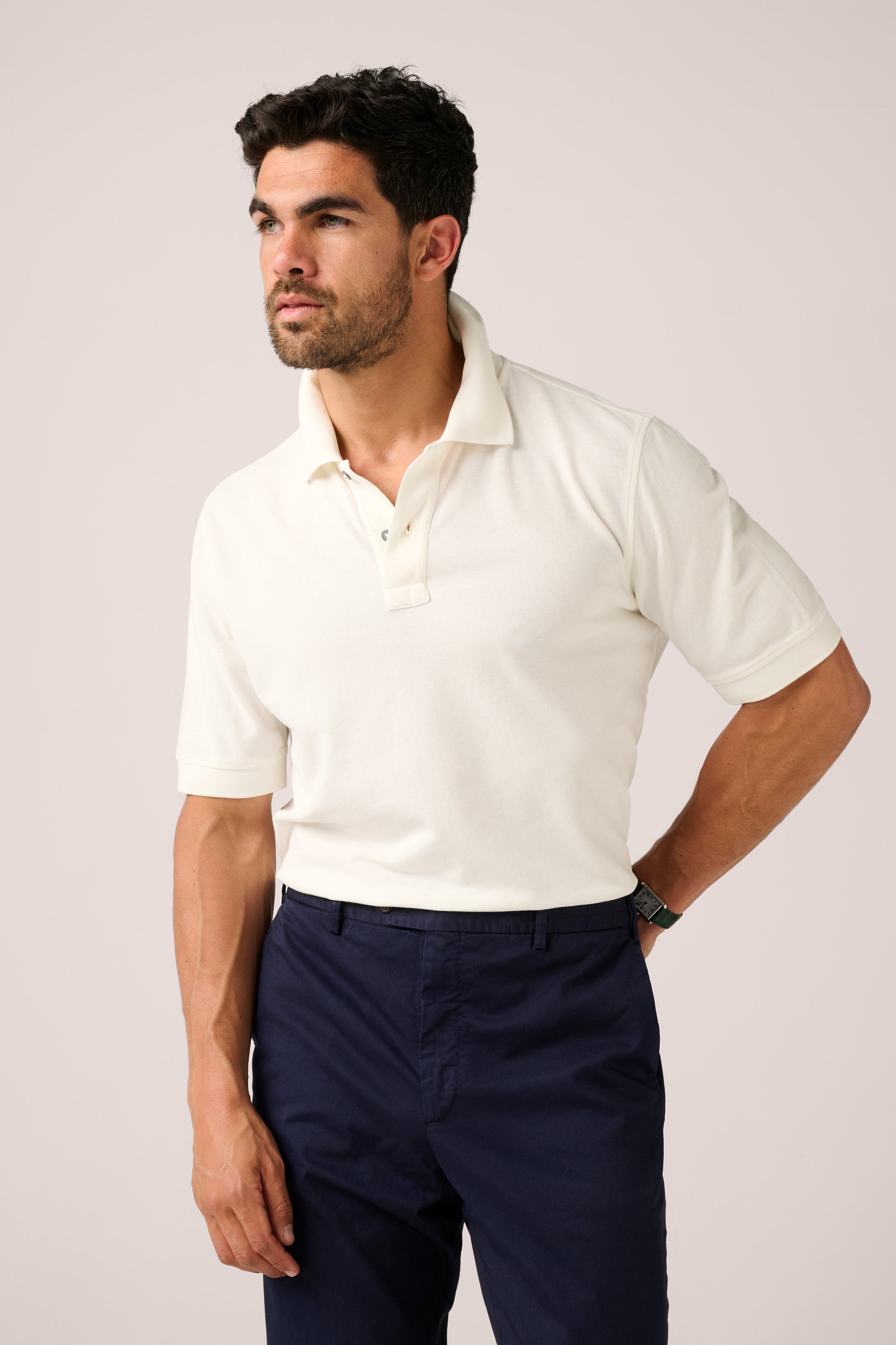 Man wearing a white polo shirt and navy pants against a plain background