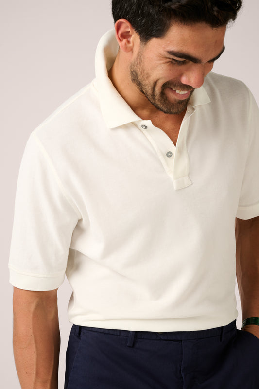 Man wearing a white polo shirt and dark pants against a plain background