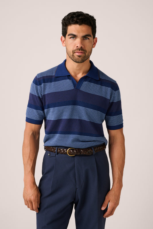 Man wearing a blue striped polo shirt and dark pants on a plain background