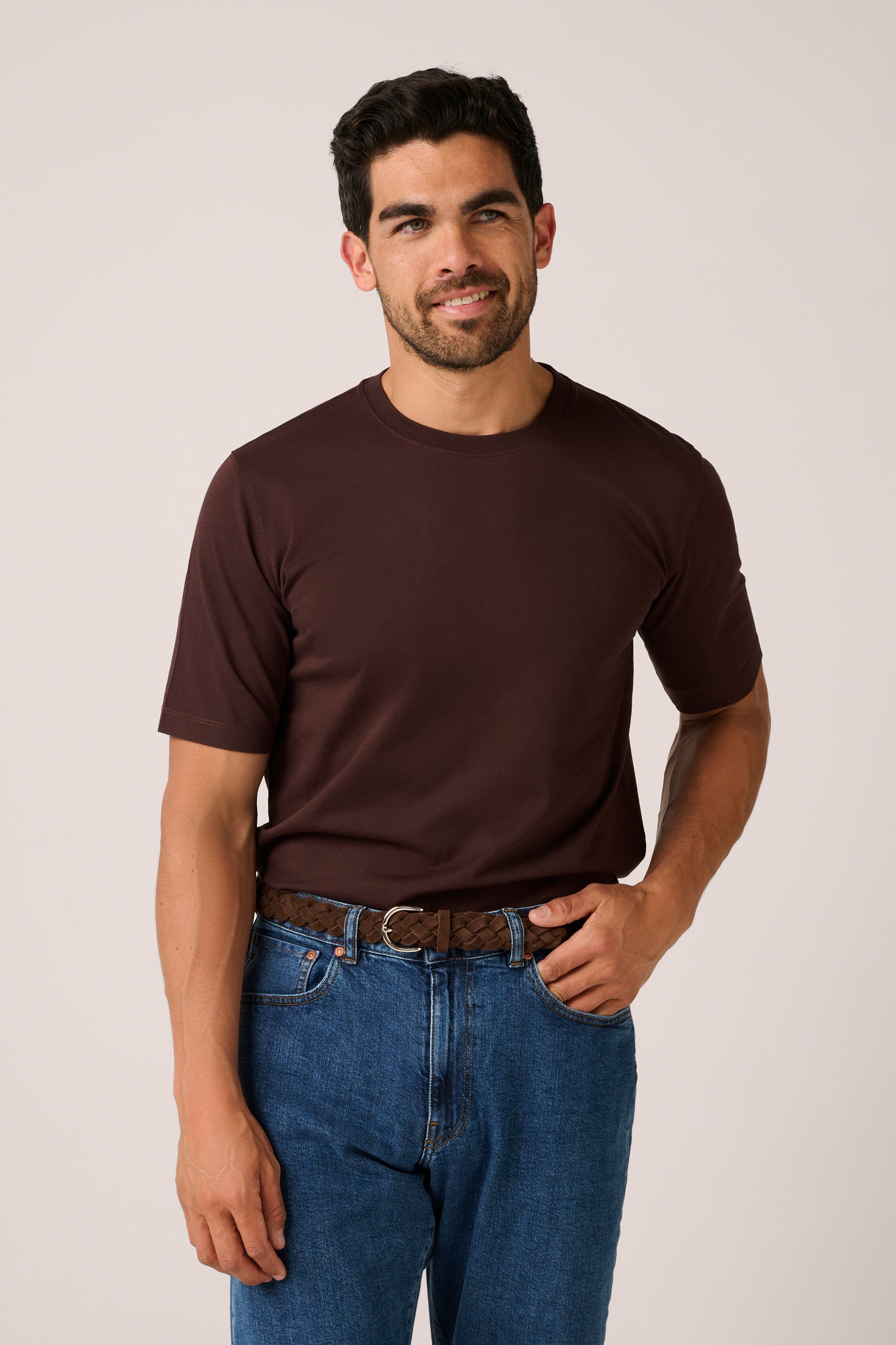 Man wearing a brown t-shirt and blue jeans against a plain background