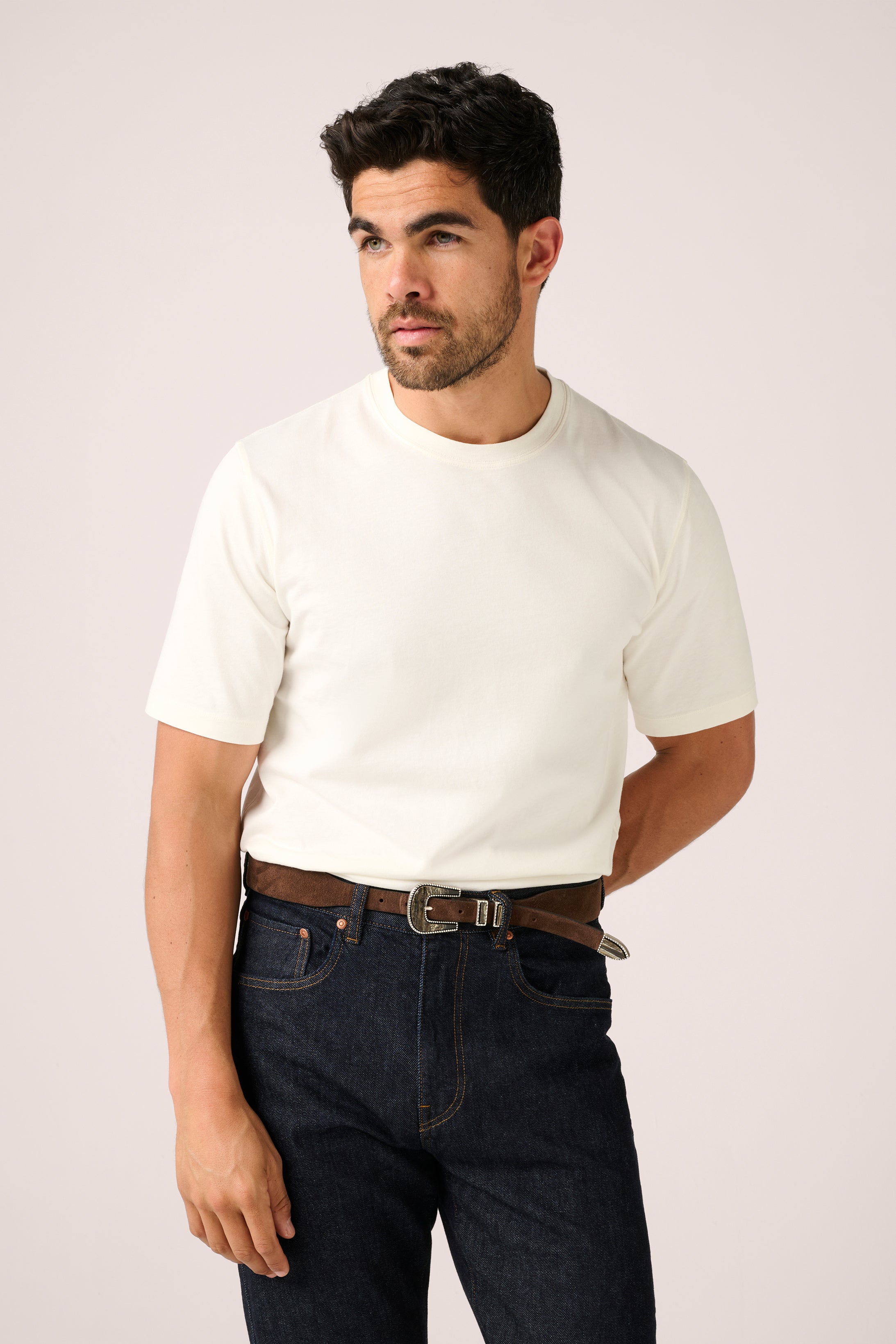 Man wearing a white t-shirt and dark jeans against a plain background