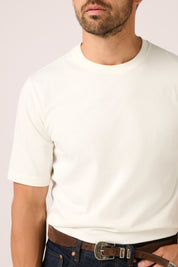 Man wearing a plain white t-shirt with a neutral background