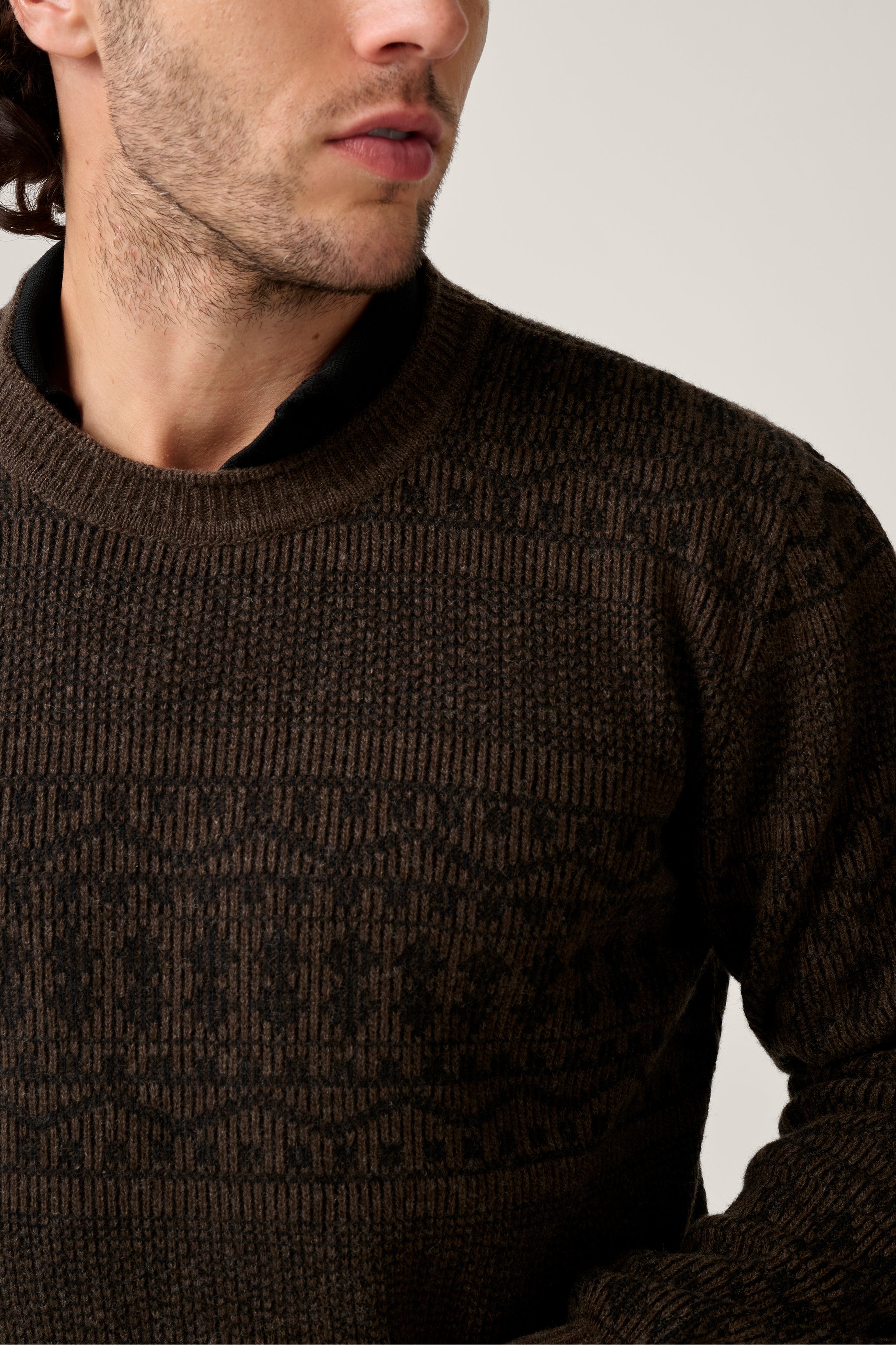 Close-up of a person wearing a brown patterned sweater against a neutral background