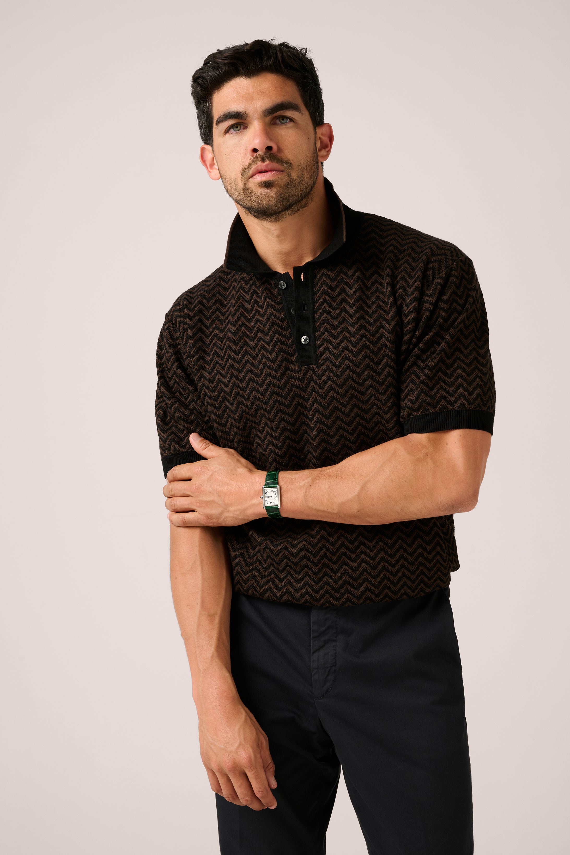 Man wearing a black patterned polo shirt against a plain background