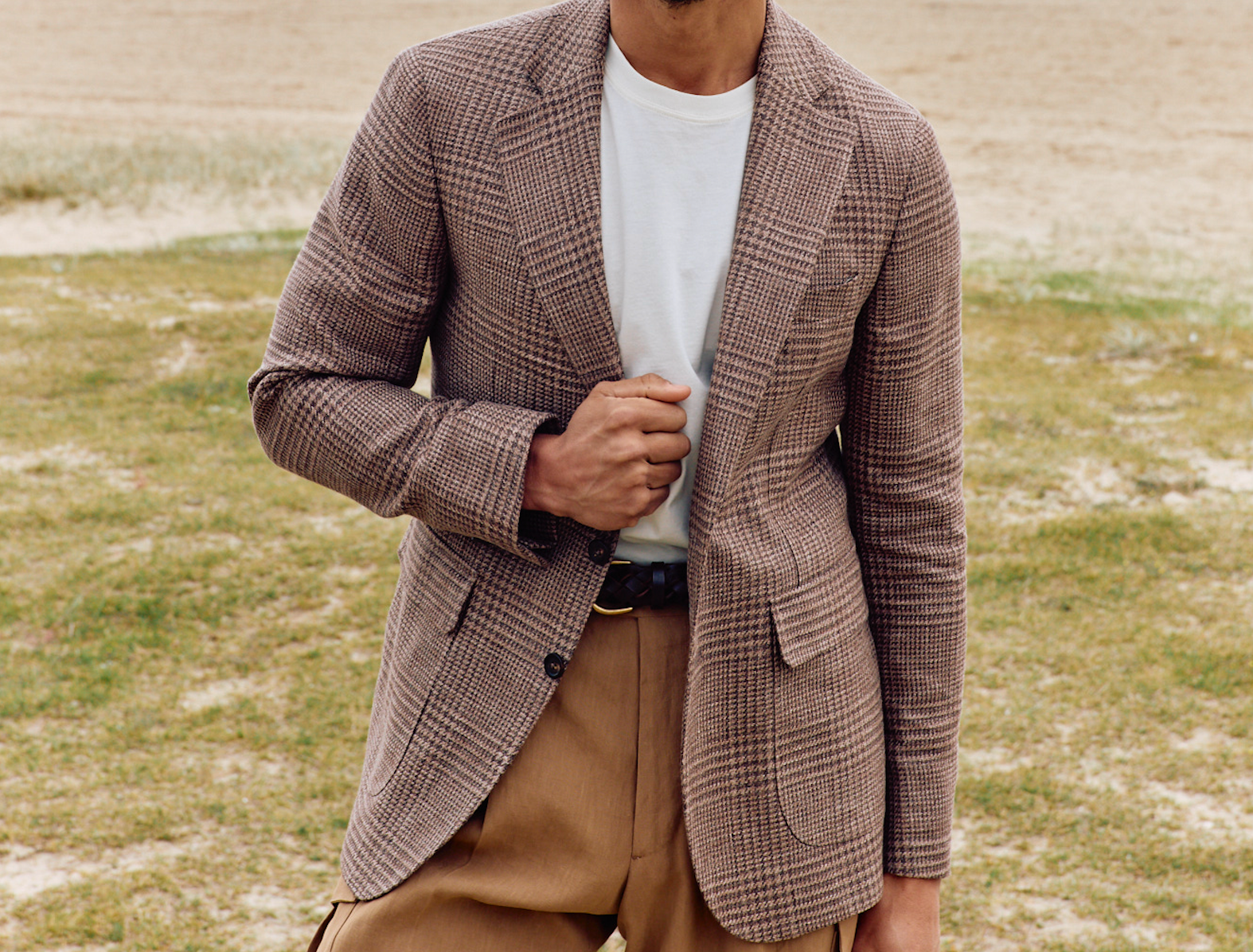 Person wearing a brown checkered blazer over a white shirt and beige pants outdoors.