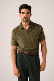 Man wearing an olive green polo shirt and dark pants on a plain background