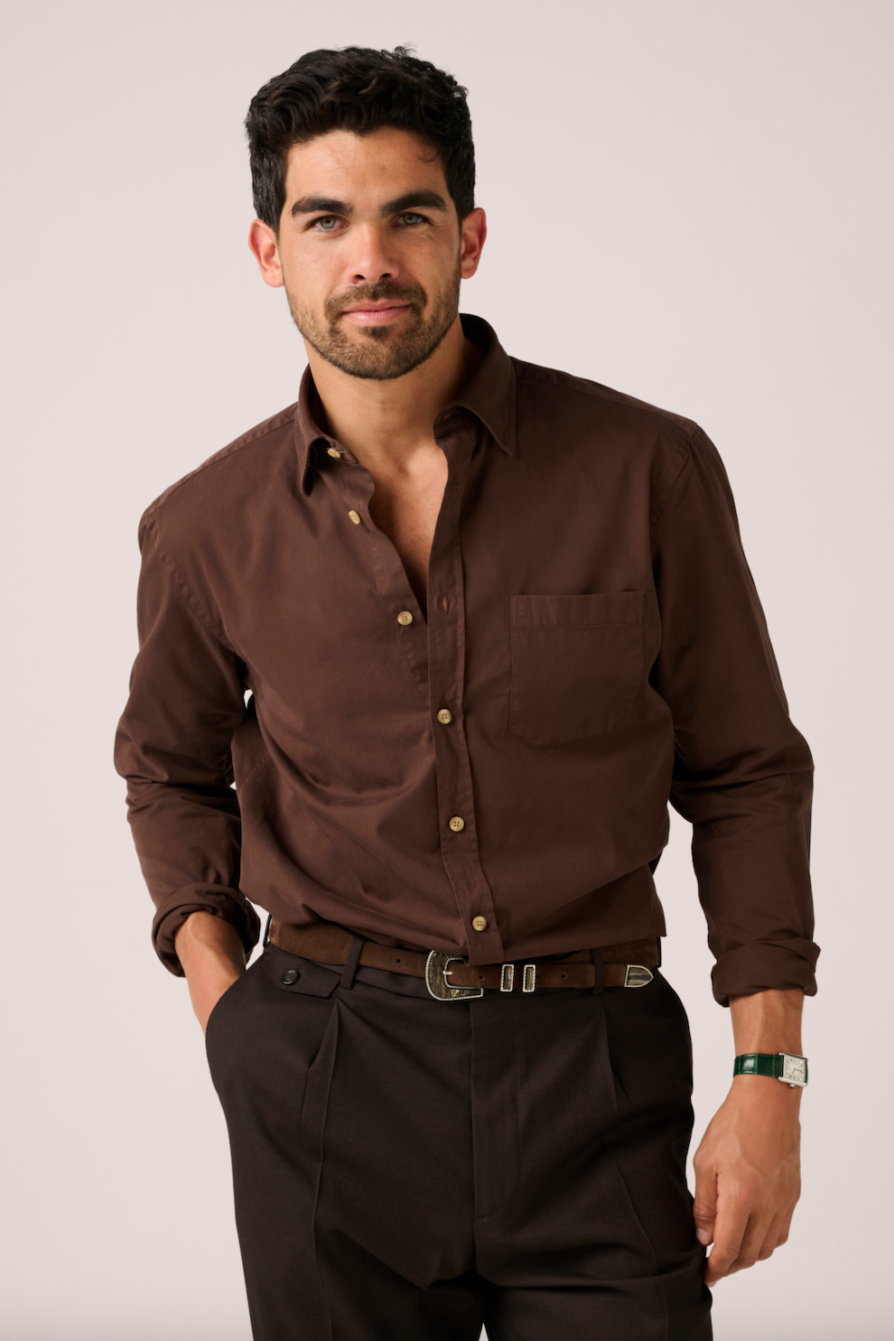 Man wearing a brown shirt and dark pants against a plain background