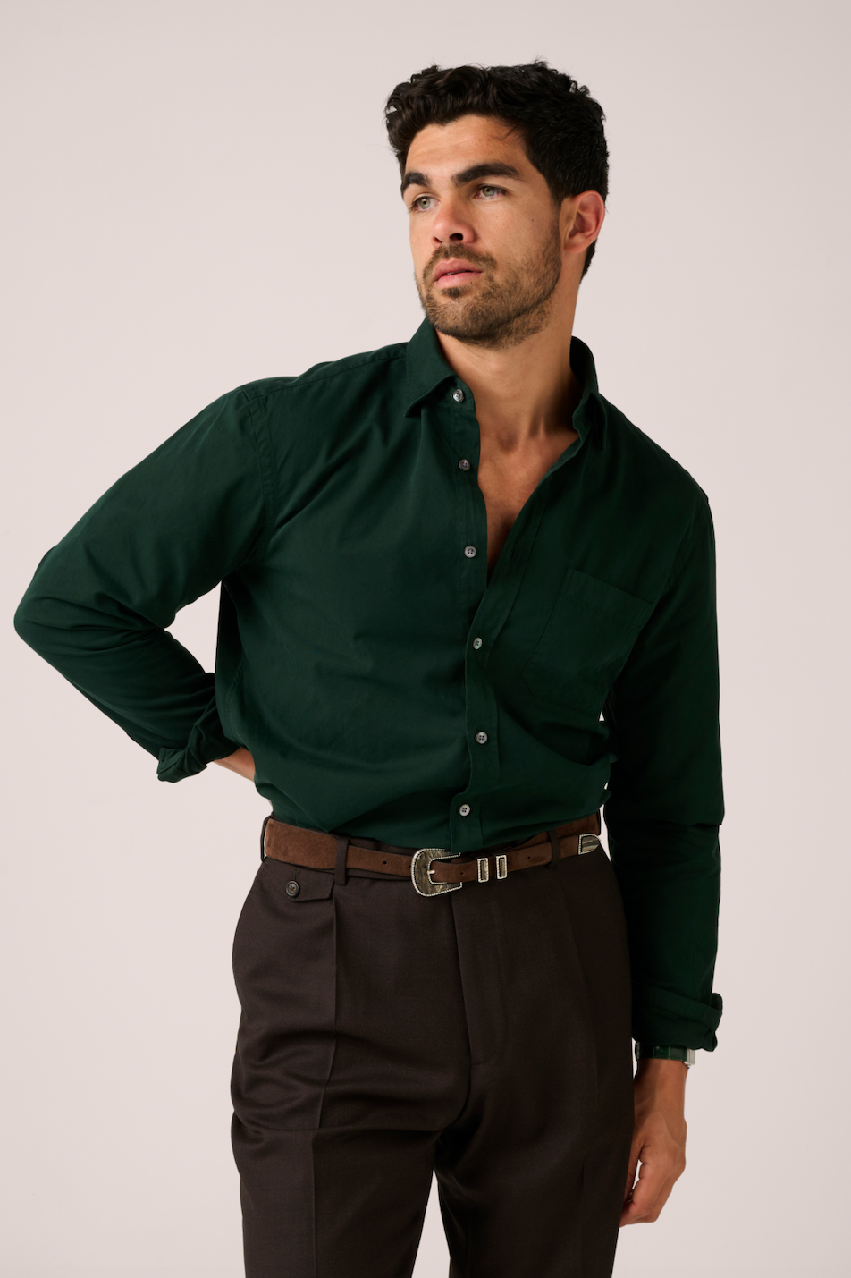 Man wearing a dark green shirt and brown pants against a plain background