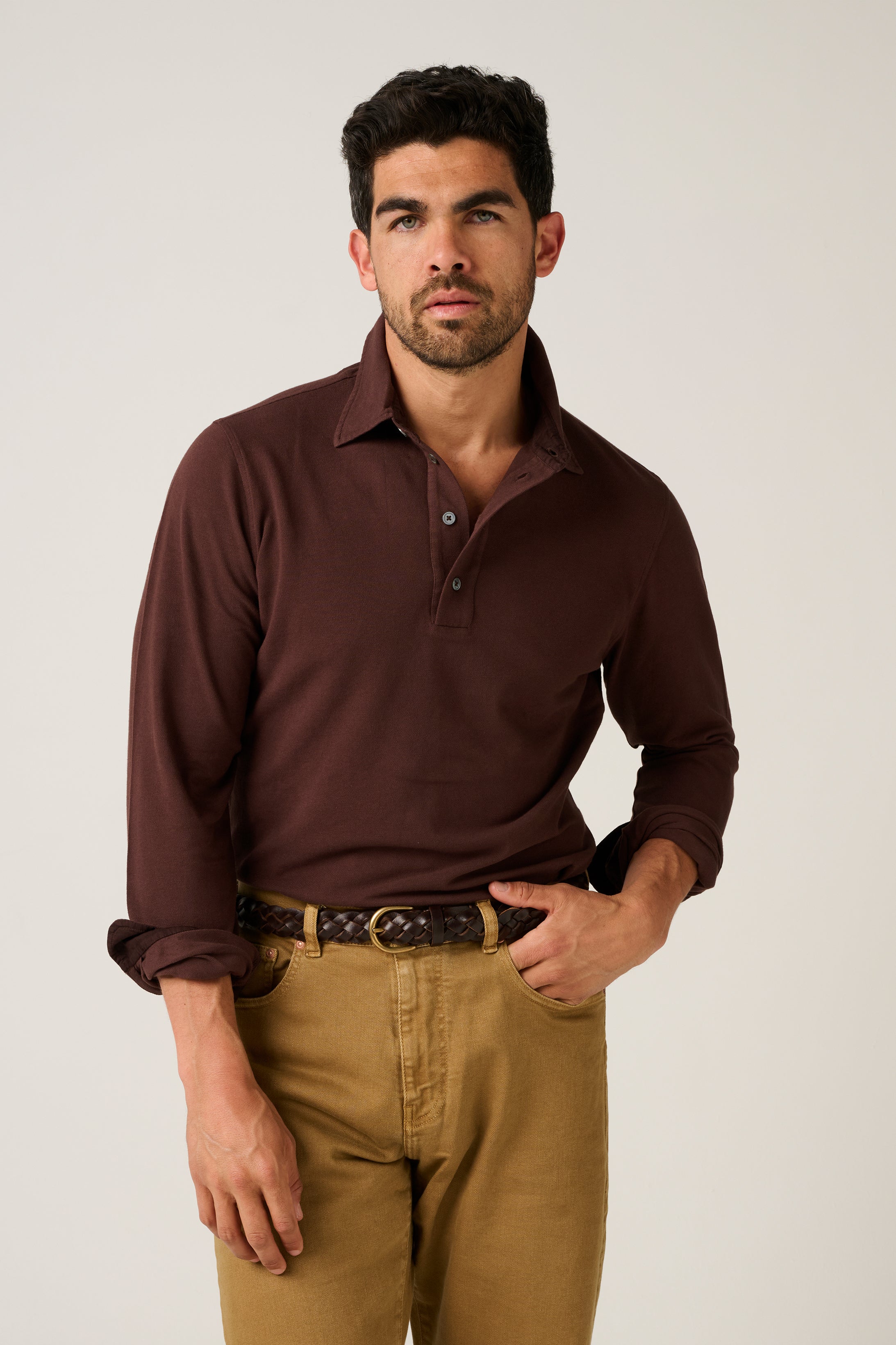 Man wearing a brown polo shirt and beige pants against a plain background