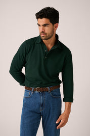 Man wearing a dark green polo shirt and blue jeans against a plain background
