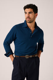 Man wearing a blue long-sleeve polo shirt and dark pants against a plain background
