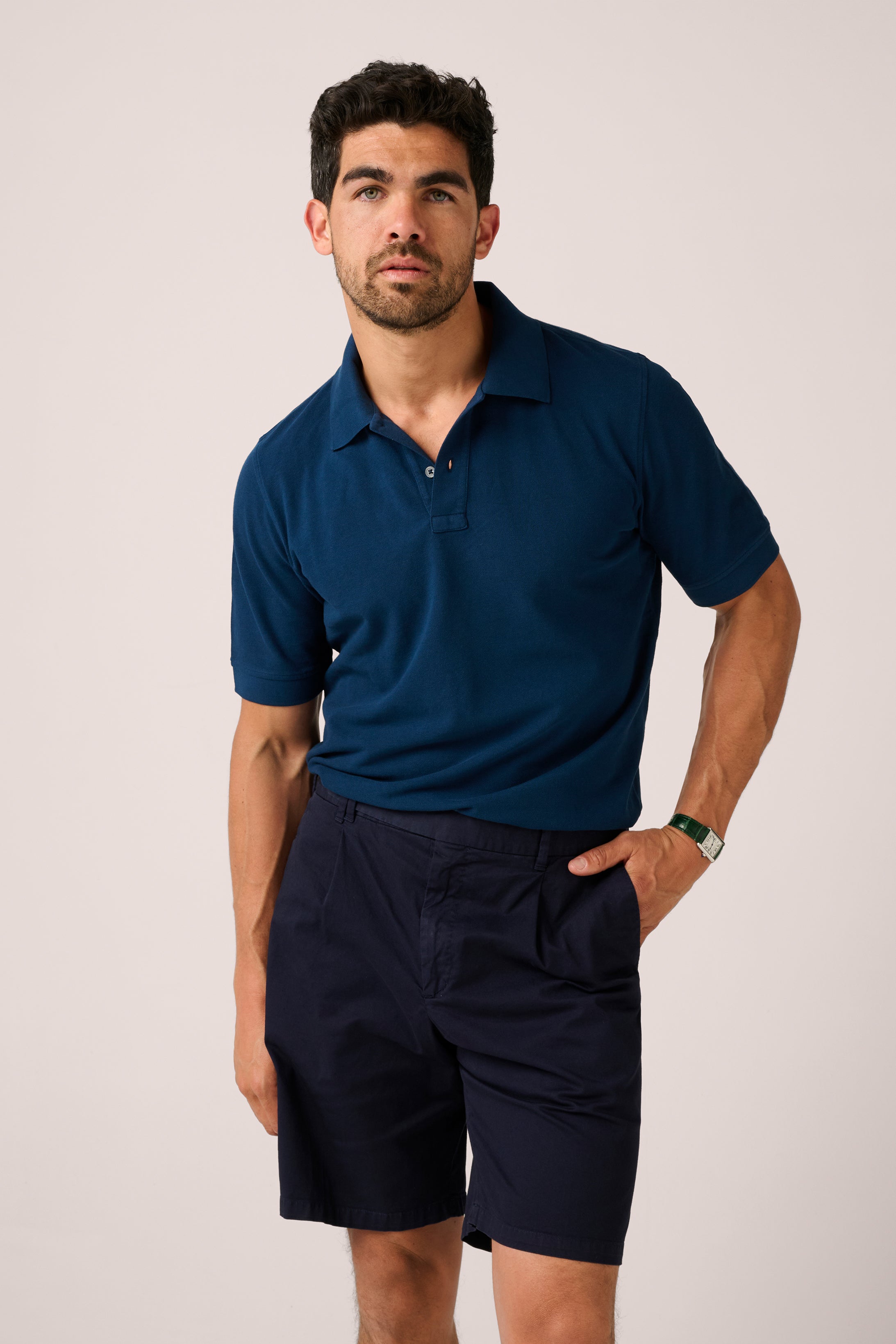 Man wearing a navy blue polo shirt and shorts on a light background