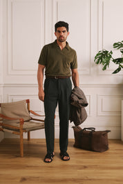 Man standing in a room with wooden floor and white paneled walls, wearing a green polo shirt and dark pants.