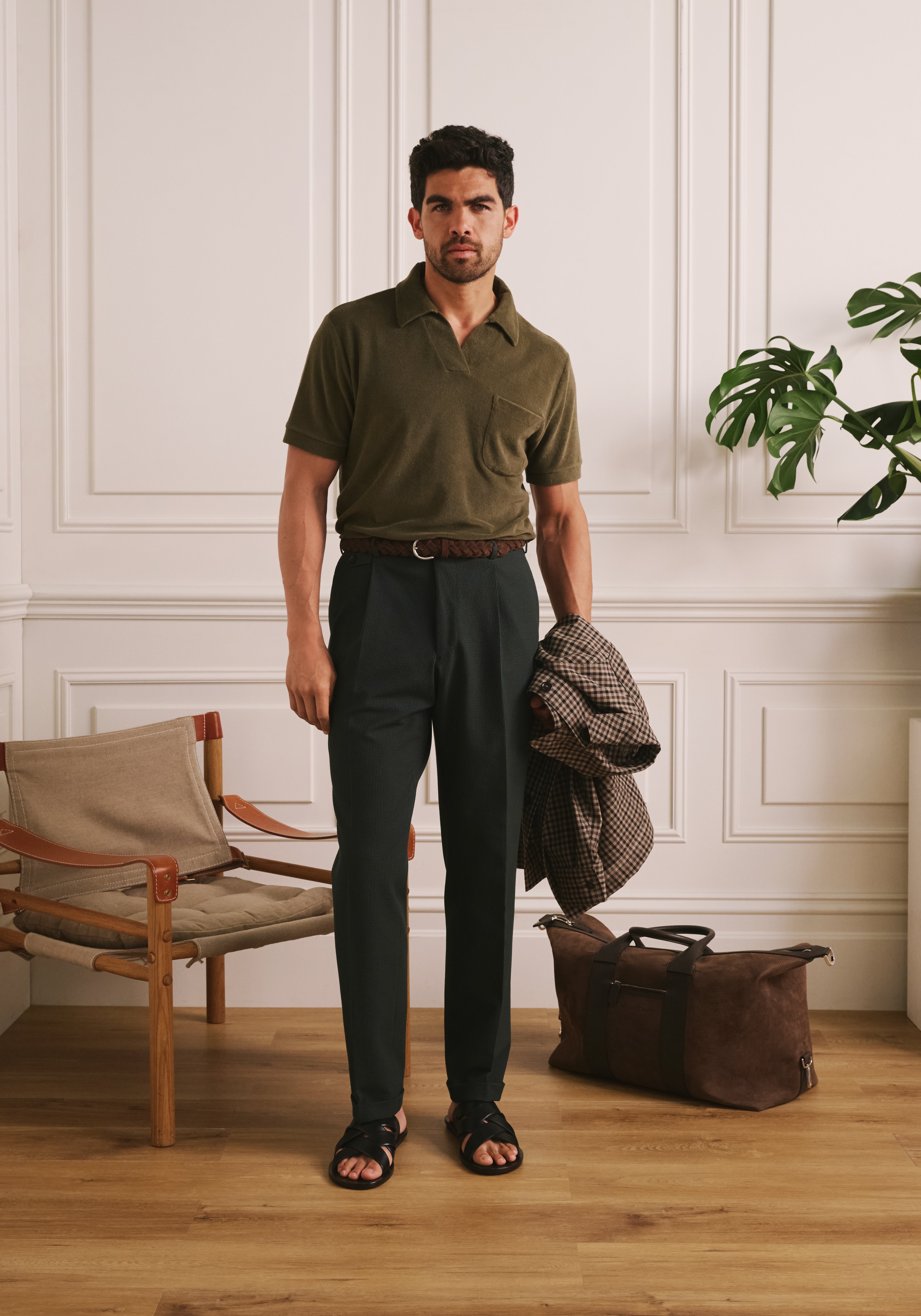 Man standing in a room with wooden floor and white paneled walls, wearing a green polo shirt and dark pants.