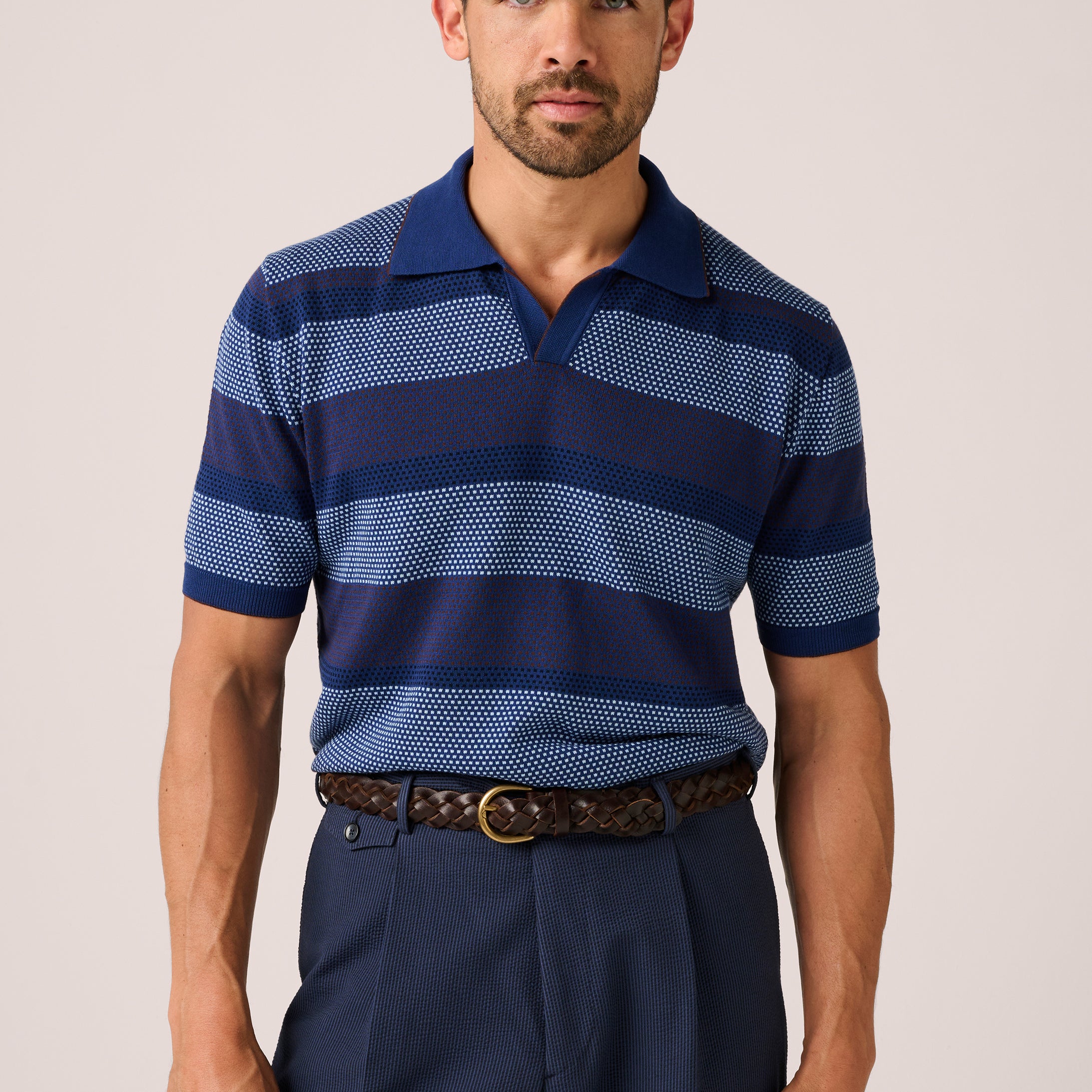 Man wearing a blue striped polo shirt and dark pants on a plain background