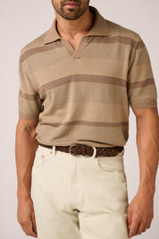Man wearing a beige patterned polo shirt and light-colored pants on a plain background