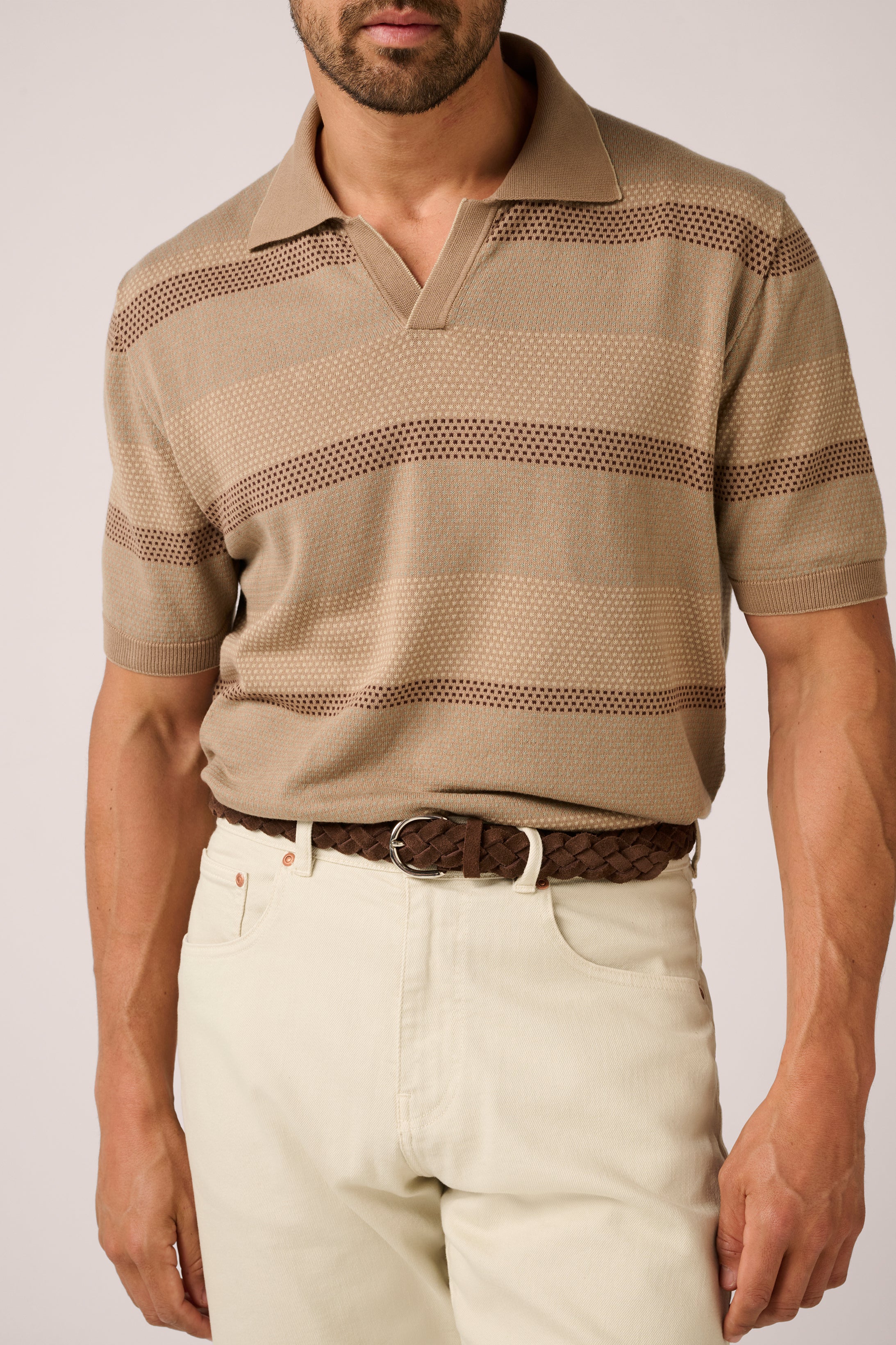 Man wearing a beige patterned polo shirt and light-colored pants on a plain background
