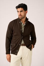Man wearing a brown jacket and white pants on a plain background