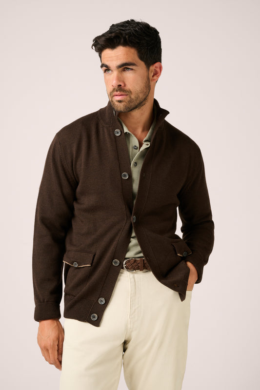 Man wearing a brown jacket and white pants on a plain background
