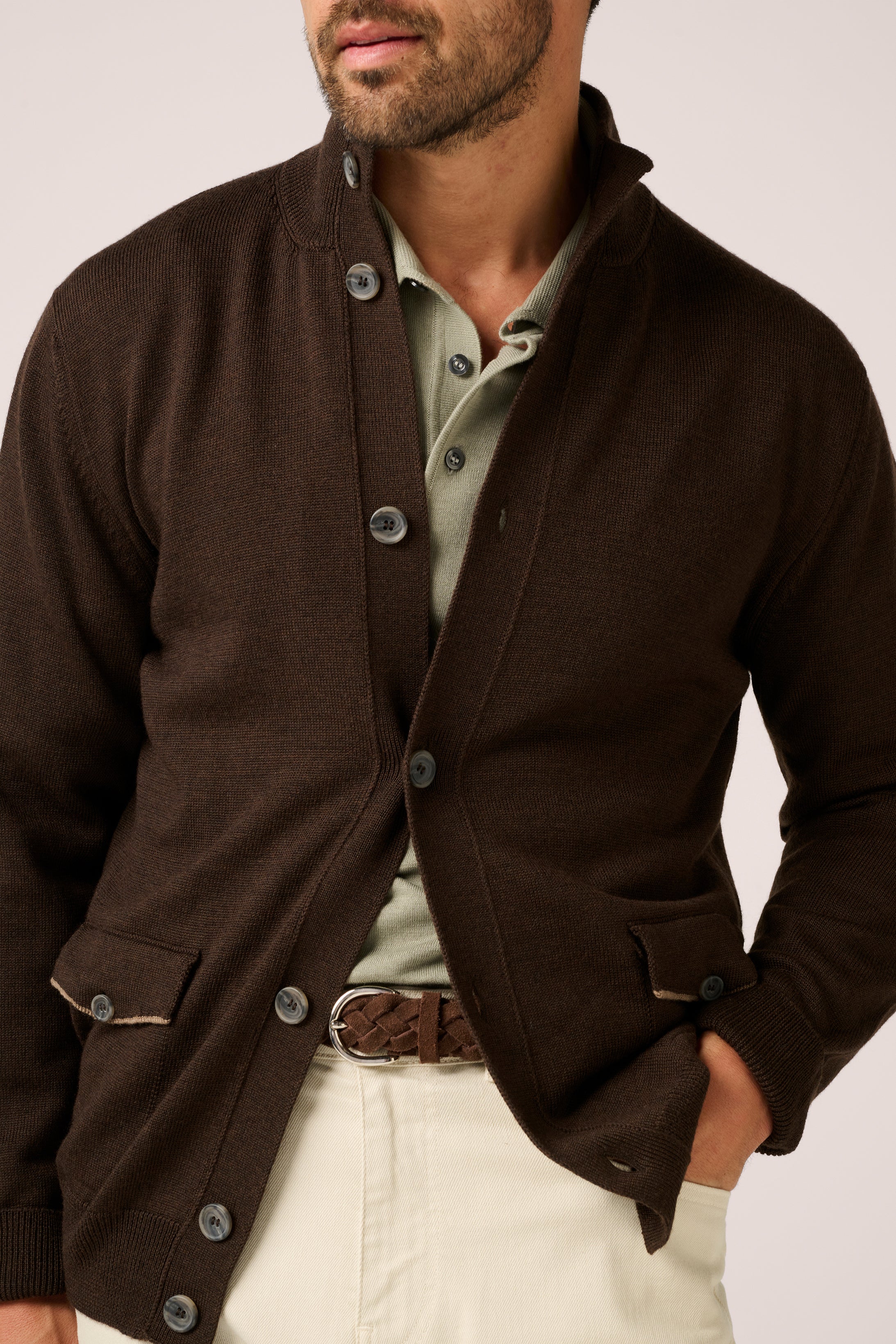 Man wearing a brown cardigan over a light shirt with a white background