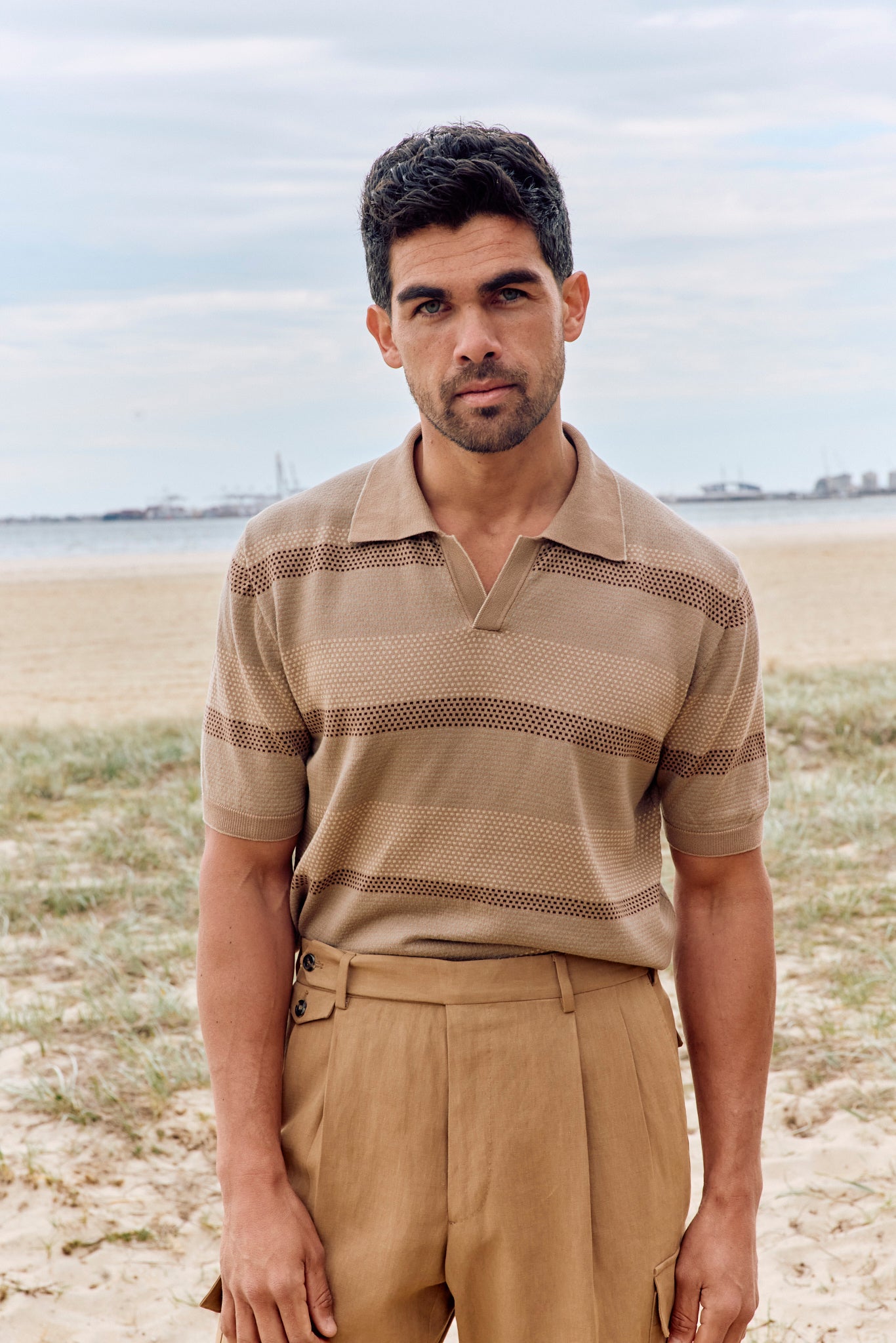 Man wearing a beige polo shirt and pants standing on a beach.