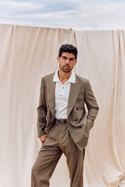Man wearing a beige suit standing against a beige curtain with a blue sky background