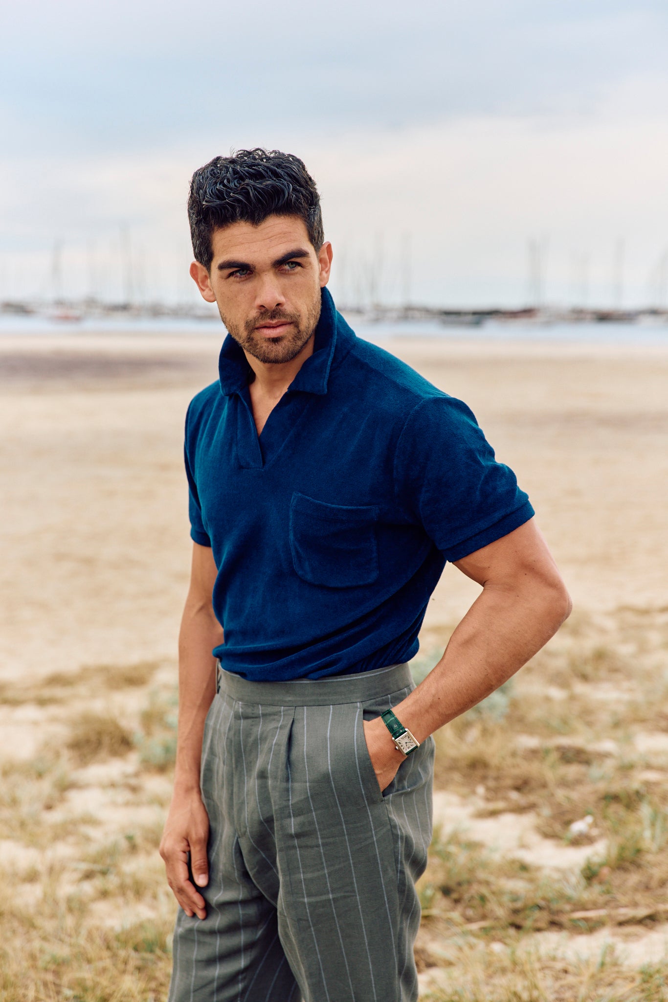 Man wearing a blue polo shirt and gray pants standing on the beach.