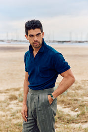 Man wearing a blue polo shirt and gray pants standing on the beach.
