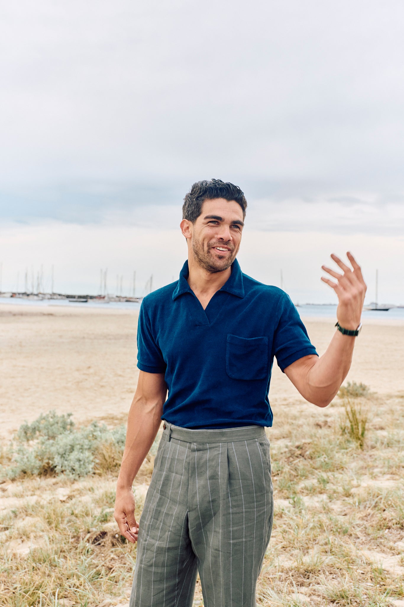 Man in a blue shirt and plaid pants standing on a beach with a cloudy sky.